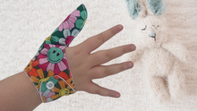 Load image into Gallery viewer, A fabric thumb guard made by The Thumb Guard Store, designed to help children and adults stop habits such as thumb sucking and skin picking. The guard in the image has a smiling flower-themed outer fabric and a moisture-resistant lining.
